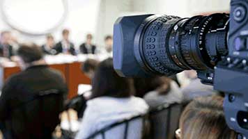 Mediacoaching voor persconferentie met shot van cameralens gericht op de sprekers achter de tafel.